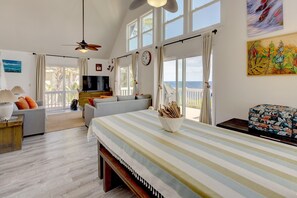 A spacious living area with a large bed, a sofa, a TV, and a balcony with a view.