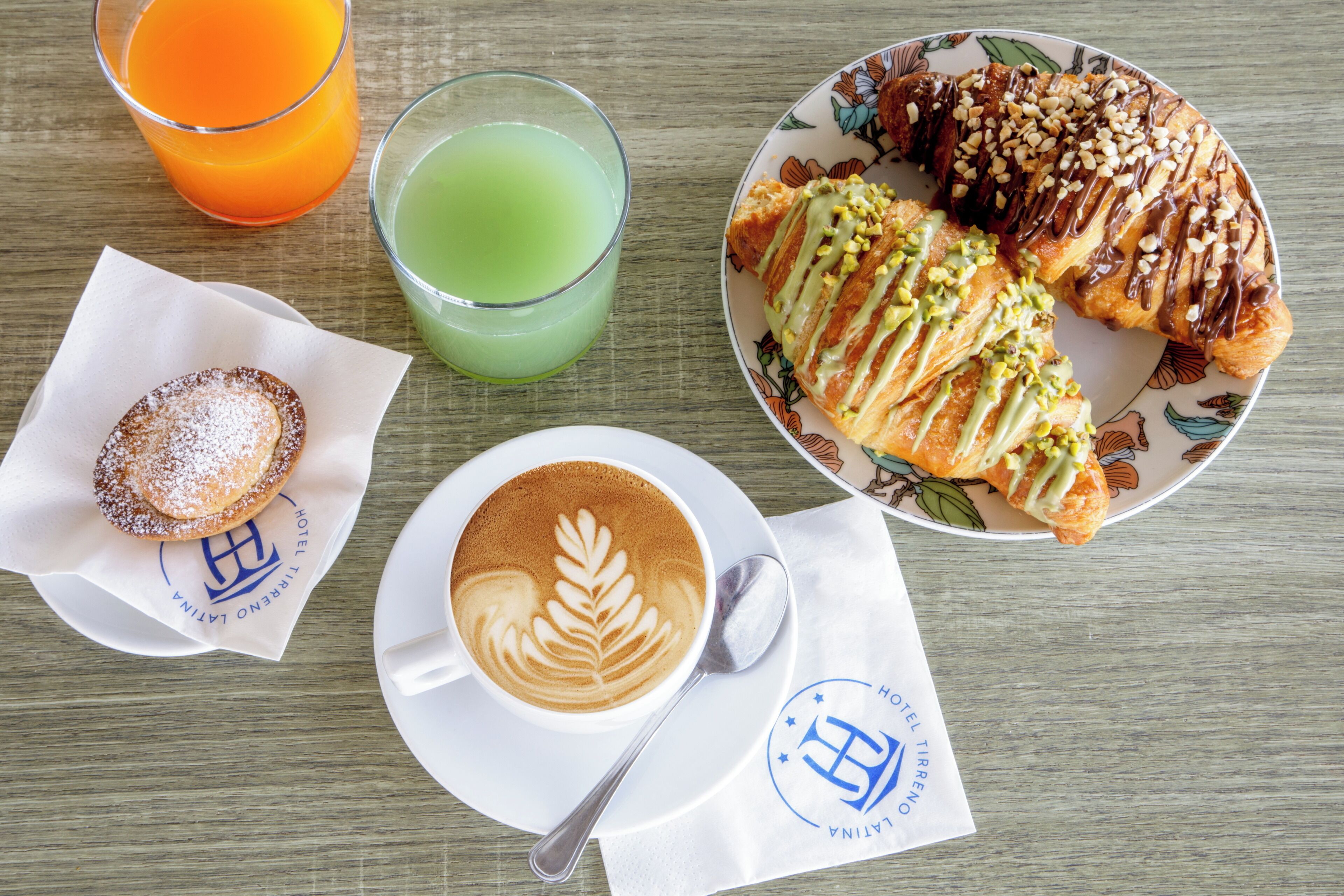 A breakfast setting with a croissant, muffin, coffee, and two drinks on a wooden table.