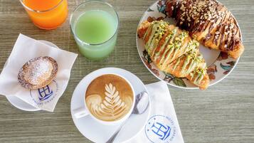 A breakfast setting with a croissant, muffin, coffee, and two drinks on a wooden table.