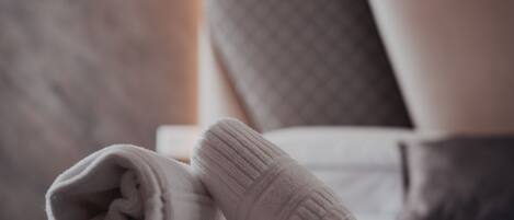 A neatly made bed with a folded white towel and a blanket, a bedside lamp, and a headboard with a textured pattern.