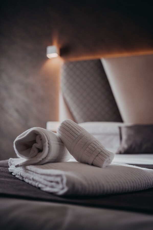 A neatly made bed with a folded white towel and a blanket, a bedside lamp, and a headboard with a textured pattern. - Hotel Tirreno (Latina)
