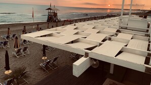 Een terras aan het strand met ligbedden en parasols, met uitzicht op de zee bij zonsondergang.
