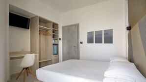 Een slaapkamer met een bed, een bureau, een stoel, een kledingkast en een televisie.