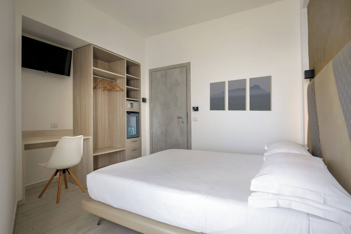 A bedroom with a bed, a desk, a chair, a wardrobe, and a television.