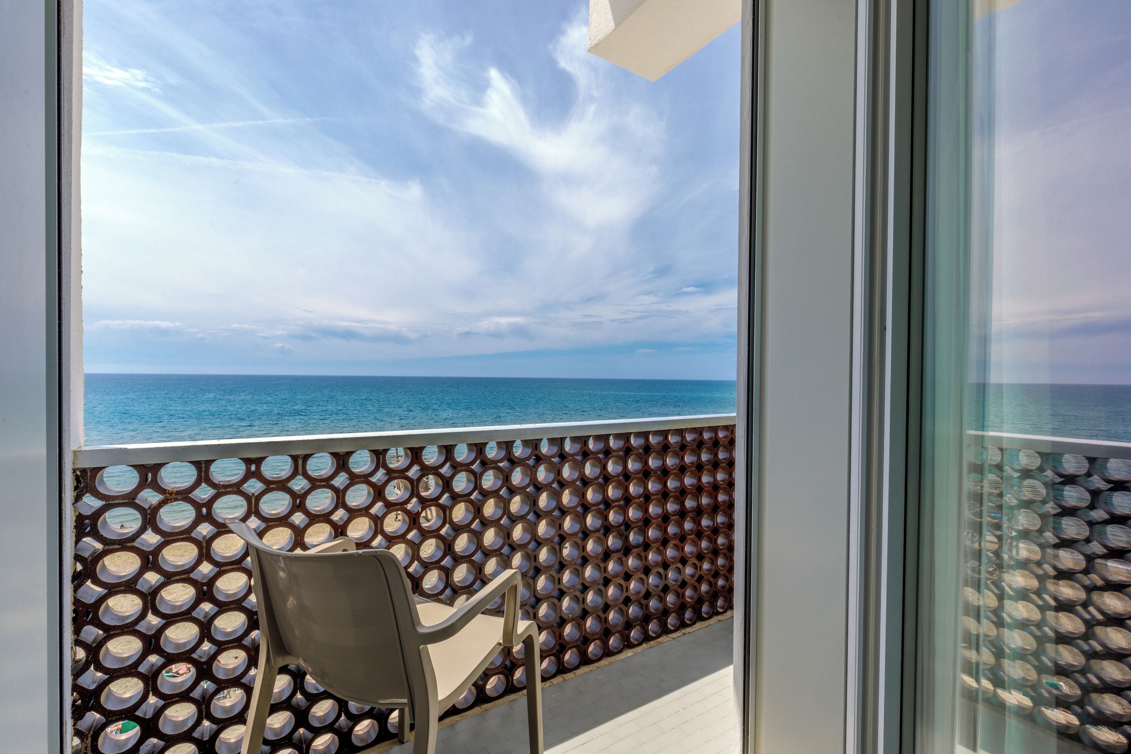 Un balcón con vista al mar, una silla y un muro con diseño.