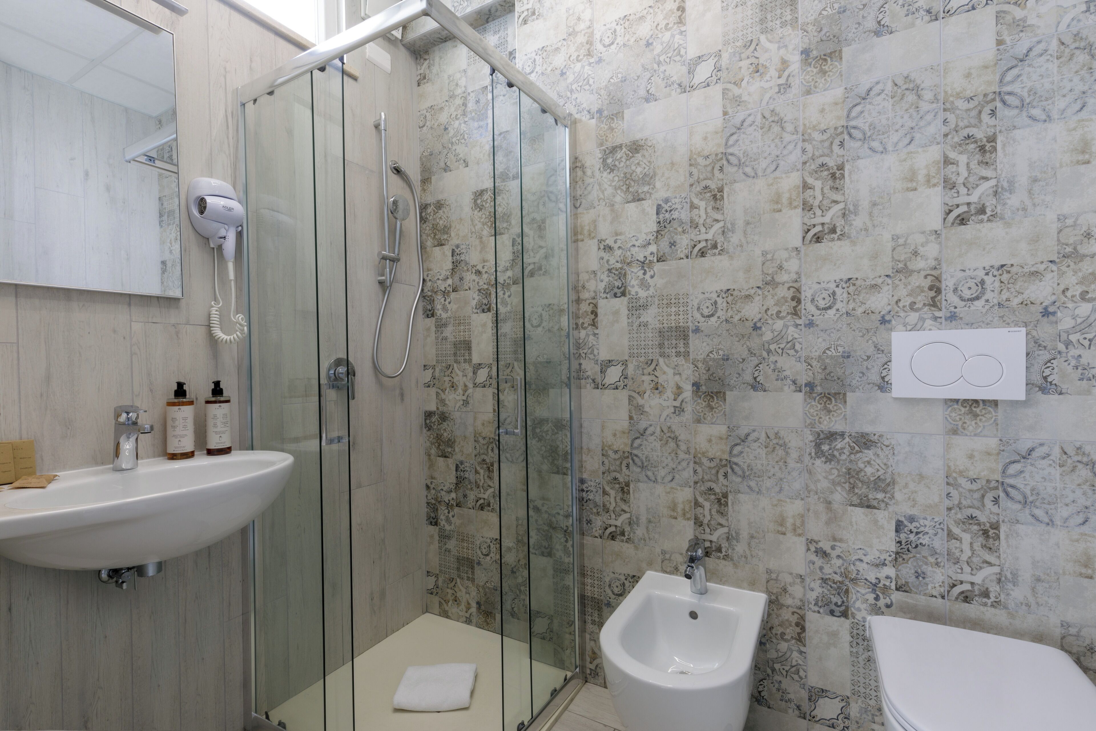 Une salle de bain dotée d’une douche à parois de verre, d’un lavabo, d’un bidet et de carreaux décorés.