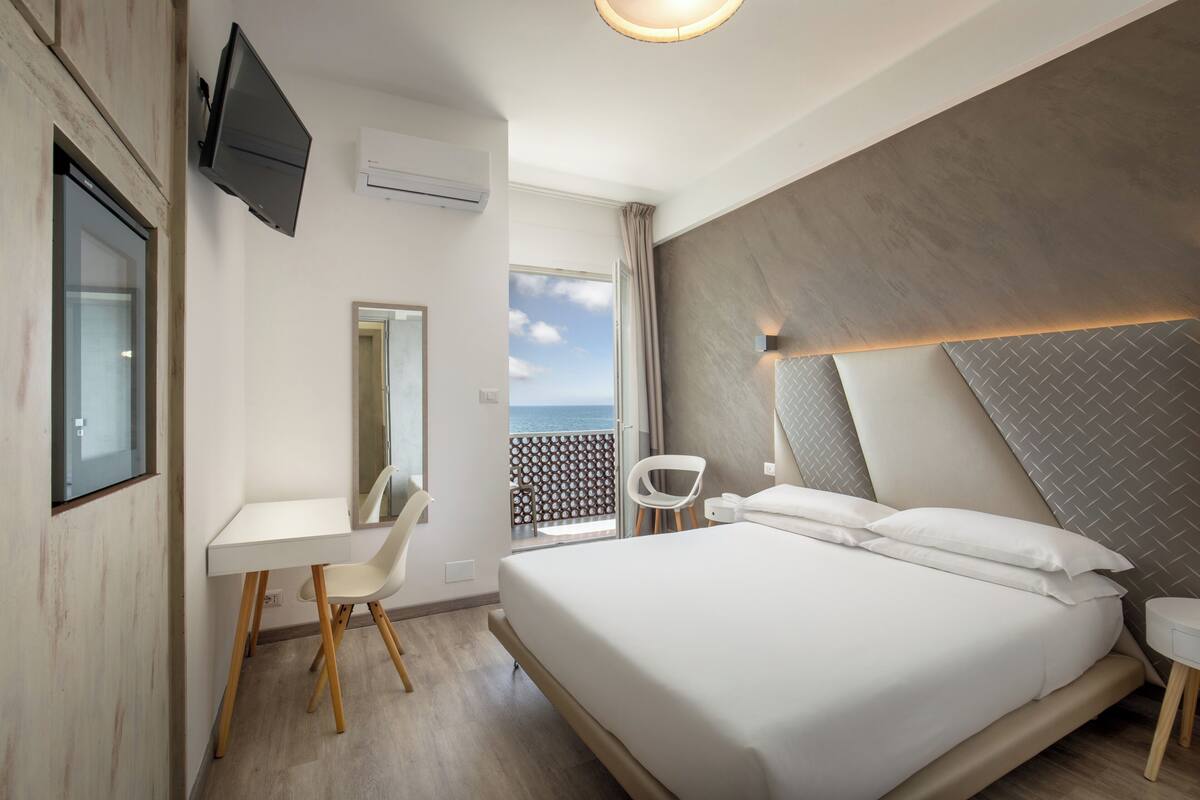 A modern hotel room with a bed, a desk, a chair, and a TV.