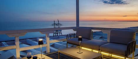 Una terraza con vistas al mar, dos sofás, una mesa con vasos y un bol, y una lámpara.