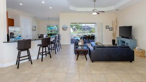 A modern living room with a sofa, a television, and a dining area with chairs and a table. - Paradise Palms - Luxury Home - Bikes & Kayaks (Cape Coral)