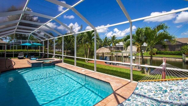 A covered swimming pool with a view of palm trees and a water feature. - Paradise Palms - Luxury Home - Bikes & Kayaks (Cape Coral)