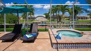 A pool area with lounge chairs and umbrellas, a hot tub, and a view of a house and palm trees. - Paradise Palms - Luxury Home - Bikes & Kayaks (Cape Coral)