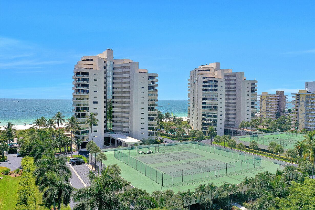 A high-rise hotel with multiple floors, a tennis court, and a view of the beach.