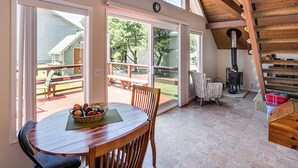 A dining area with a wooden table and chairs, a basket of fruit, and a view of the outdoors through large sliding glass doors. - Romantic A-Frame Beach Cottage, Blocks to the Beach, Deck, Fireplace and Firepit (Rockaway Beach)