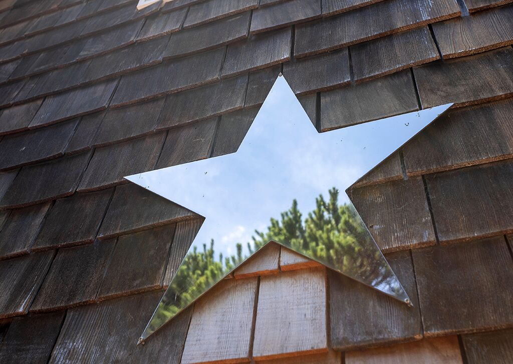 A star-shaped mirror reflecting a building's roof and trees.