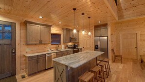 A modern kitchen with wooden cabinetry, stainless steel appliances, and a central island with bar stools. - Misty Mountain Adventure Lodge: 180 Degree views (Gatlinburg)