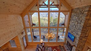 A log cabin interior with a large window offering a mountain view, a fireplace, and a cozy seating area. - Misty Mountain Adventure Lodge: 180 Degree views (Gatlinburg)