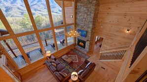 A spacious living room with a fireplace, large windows, and a cozy seating area. - Misty Mountain Adventure Lodge: 180 Degree views (Gatlinburg)