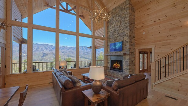 A spacious living room with a stone fireplace, large windows offering mountain views, and a cozy seating area. - Misty Mountain Adventure Lodge: 180 Degree views (Gatlinburg)