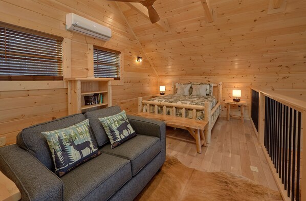 A cozy cabin room with a bed, a sofa with decorative pillows, a small table, and a bookshelf. - Misty Mountain Adventure Lodge: 180 Degree views (Gatlinburg)