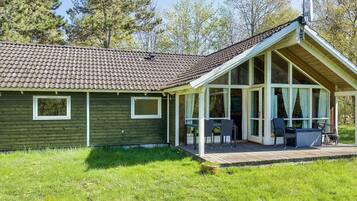A single-story house with a sloped roof, a covered porch with outdoor seating, and a satellite dish.
