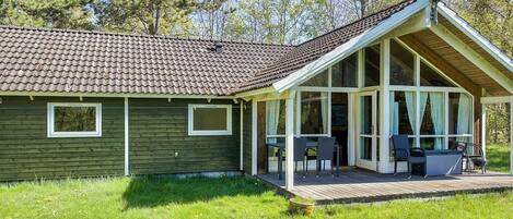 Une maison de plain-pied avec un toit en pente, une véranda couverte avec des sièges d’extérieur et une antenne parabolique.