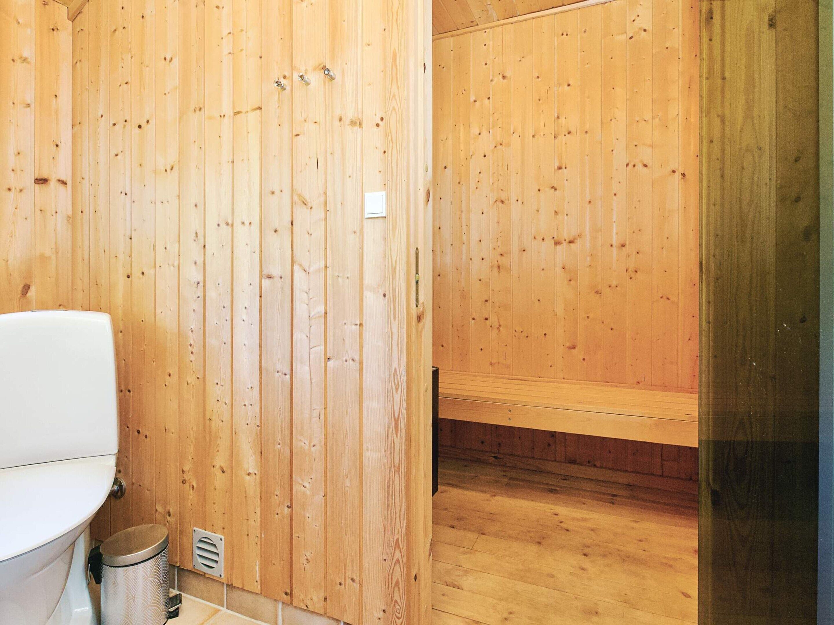 Een houten badkamer met toilet, prullenbak en bankje.