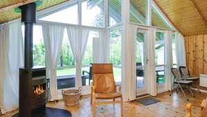 A cozy cabin interior with a wood-burning stove, large windows, a wooden ceiling, and a comfortable seating area. - 6 Person Holiday Home in Vig (Vig)