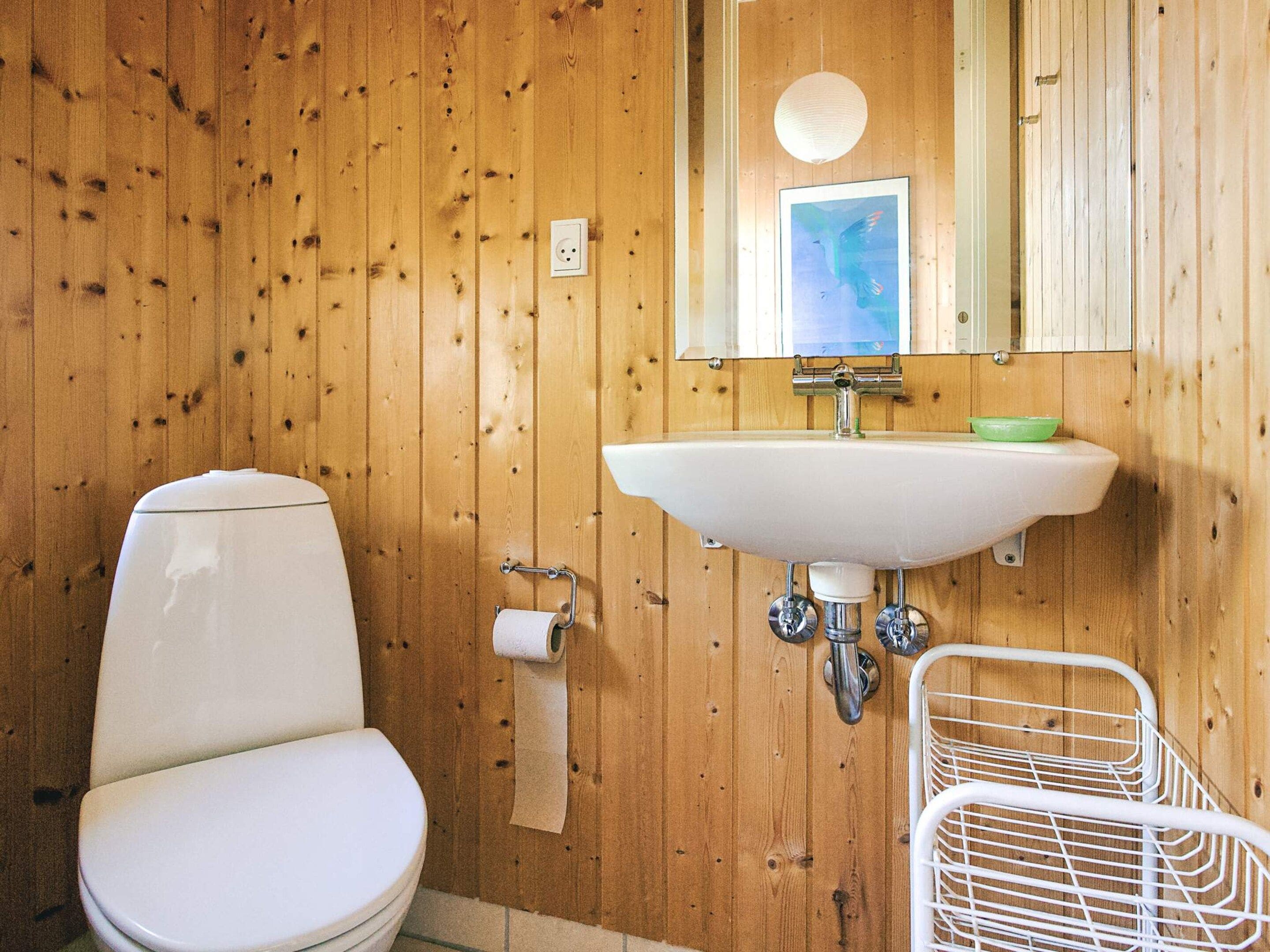 A wooden-paneled bathroom with a white toilet, a sink, and a mirror.