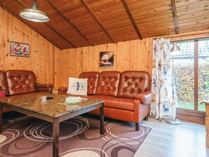 Une pièce chaleureuse avec un décor intérieur en bois, un canapé en cuir, une table basse et une grande fenêtre avec des rideaux.