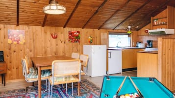 Un interior de madera con mesa de billar, mesa de comedor, sillas, refrigerador y zona de cocina.