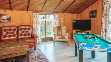 Un interior de madera con sofá, sillón, televisor y mesa de billar.