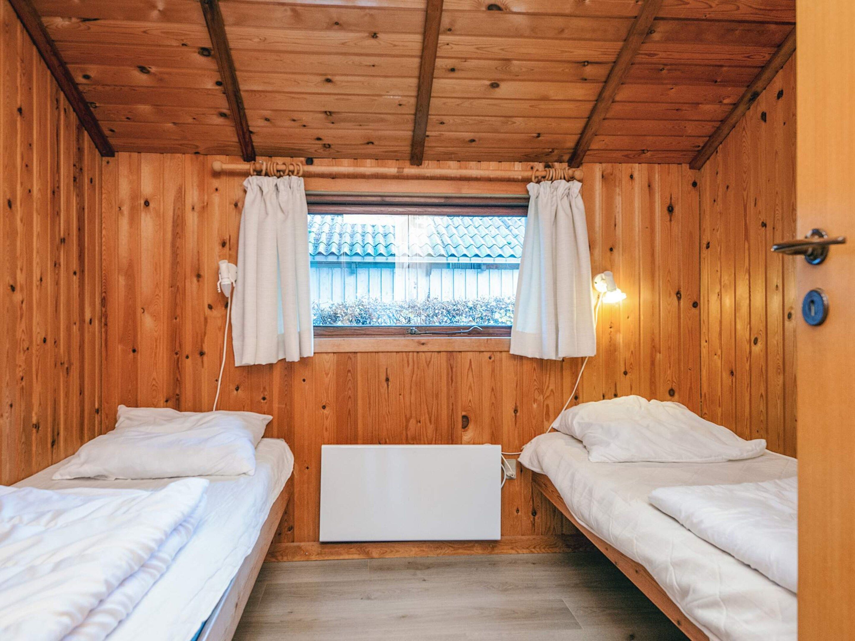Habitación con dos camas, paredes de madera, una ventana con cortinas y una lámpara fijada a la pared.