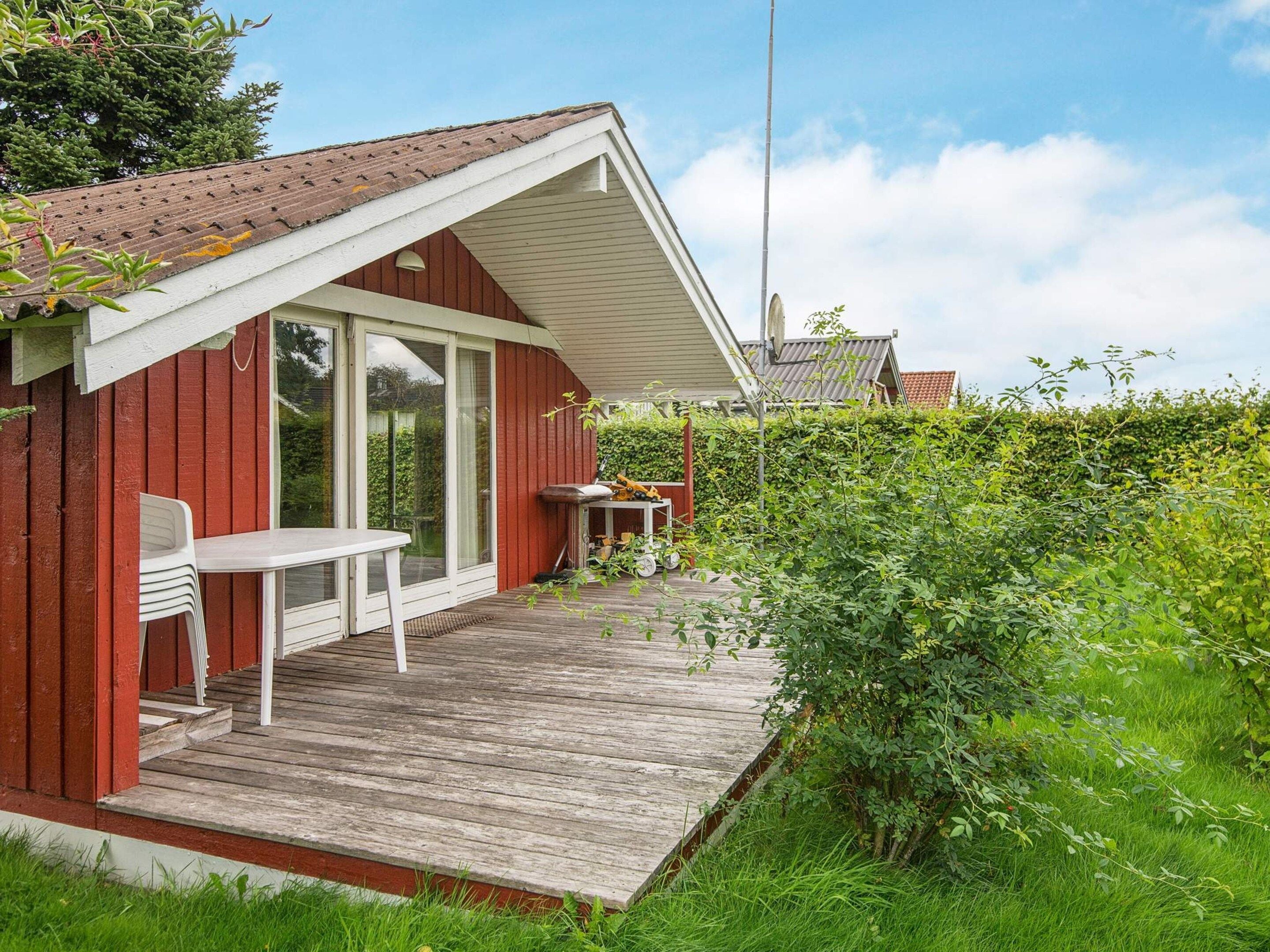 A red wooden building with a covered patio, a table, and a chair.