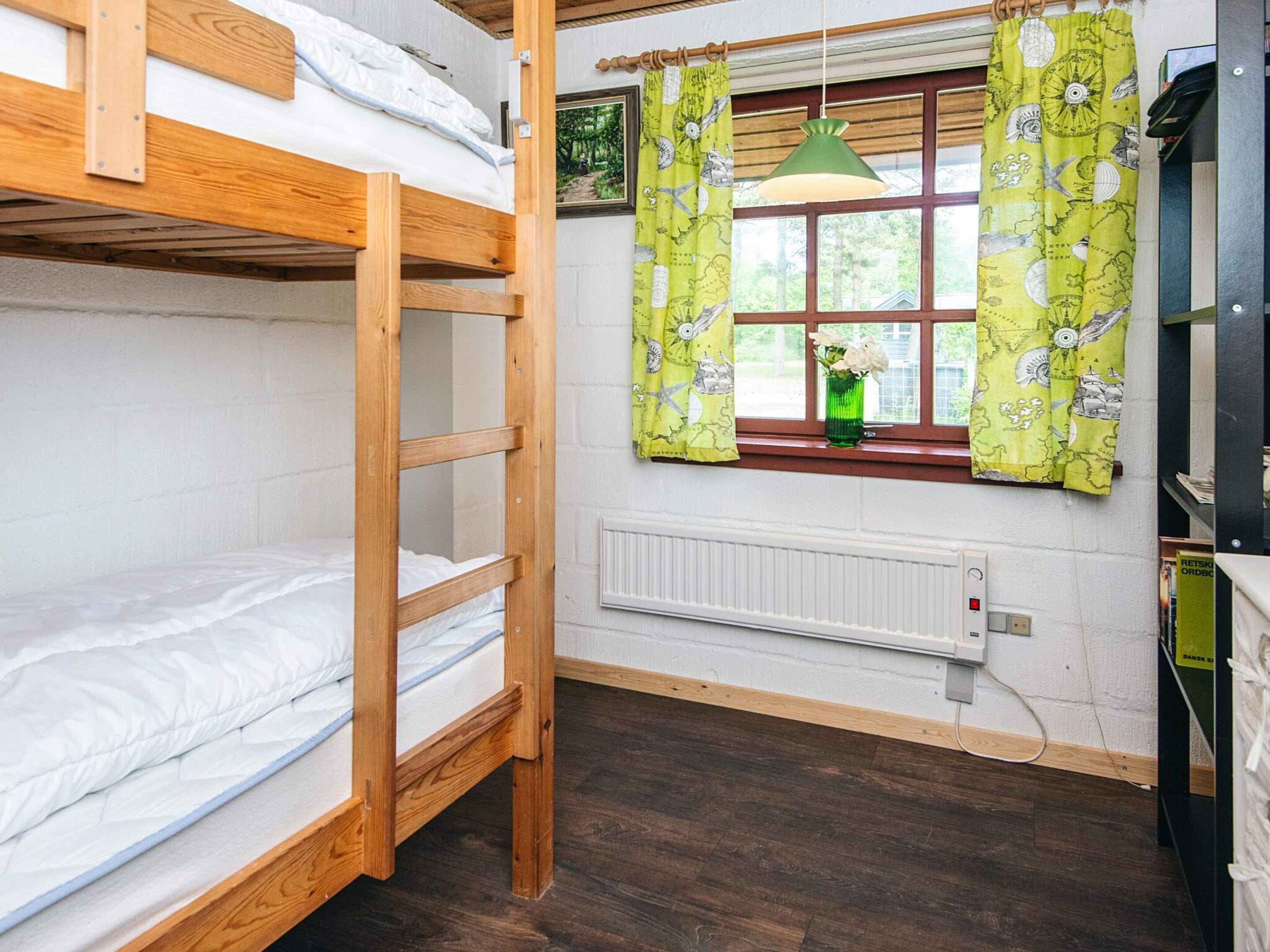 A dormitory room with bunk beds, a window with curtains, a radiator, and a hanging light fixture.