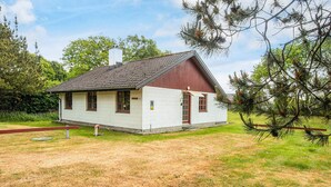 Ett litet hus i en våning med rött tak och vita väggar, omgivet av träd och gräs.