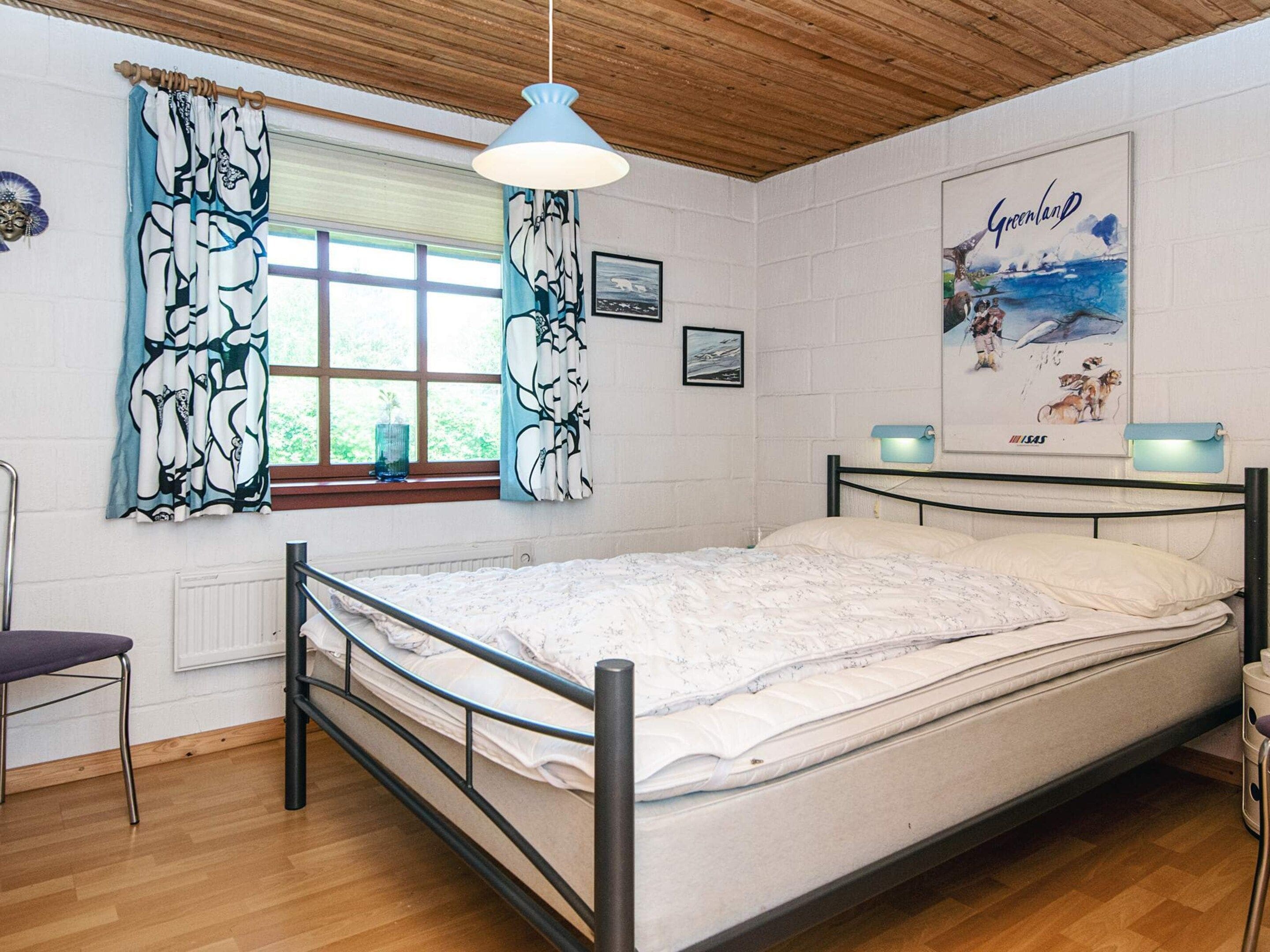 Une chambre à coucher avec un lit, une fenêtre avec des rideaux, une affiche accrochée au mur et une chaise.