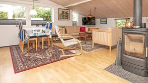 Un salon chaleureux avec un plafond en bois, une cheminée, un coin repas avec des chaises et une table, et un canapé.