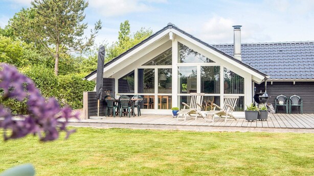 Une maison avec une grande façade vitrée, une terrasse en bois et une cheminée.