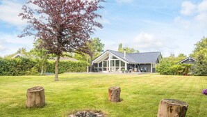 Une maison avec une grande pelouse, un arbre et un espace barbecue.
