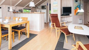 Une cuisine moderne avec des meubles en bois, un coin repas avec une table et des chaises en bois, un salon avec un téléviseur et des œuvres d’art, et un plafond de style industriel avec des poutres apparentes.