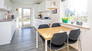 A modern kitchen with white cabinets, a wooden dining table, and black chairs. - Enticing Holiday Home in Jutland near Sea (Aalbaek)