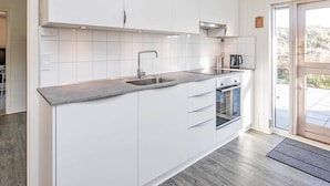 A modern kitchen with white cabinets, a stainless steel sink, and an oven. - Enticing Holiday Home in Jutland near Sea (Aalbaek)