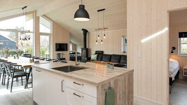 A modern kitchen with a central island, wooden cabinets, and a built-in stove. - 14 Person Holiday Home in Vaeggerlose (Vaeggerlose)