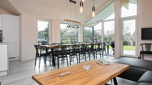 A modern kitchen with white cabinets, a dining area with a wooden table and chairs, and a large sliding glass door leading to a garden. - 14 Person Holiday Home in Vaeggerlose (Vaeggerlose)