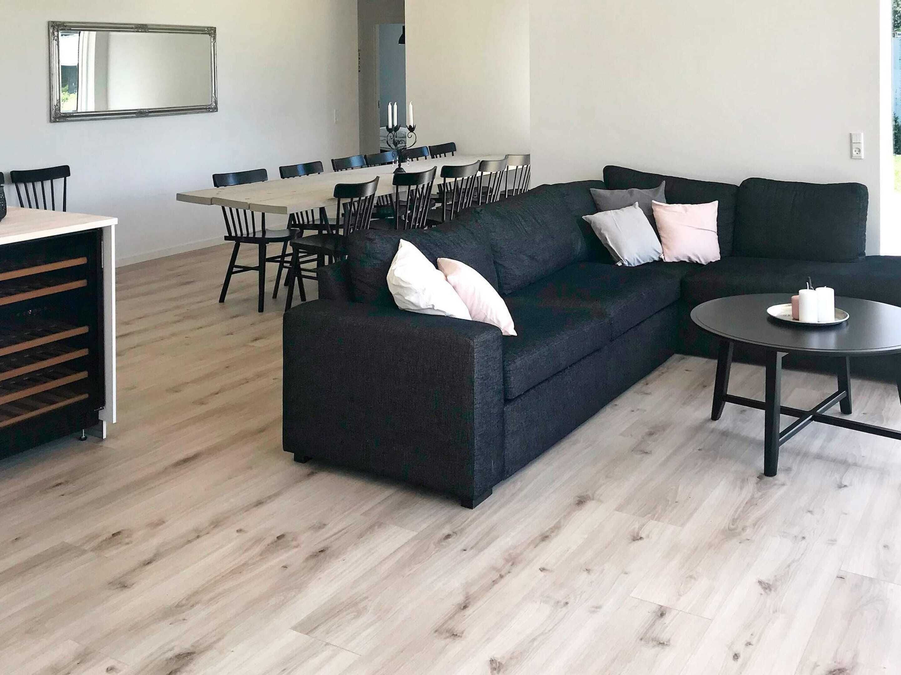 A modern living room with a dark sofa, a dining table with chairs, and a small round table with a candle.