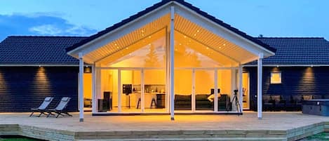 A covered outdoor area with a glass enclosure, a wooden deck, and a lawn.
