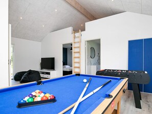 A pool table with balls and cues, a television, a bed, and a wardrobe in a room with white walls and a wooden ceiling.