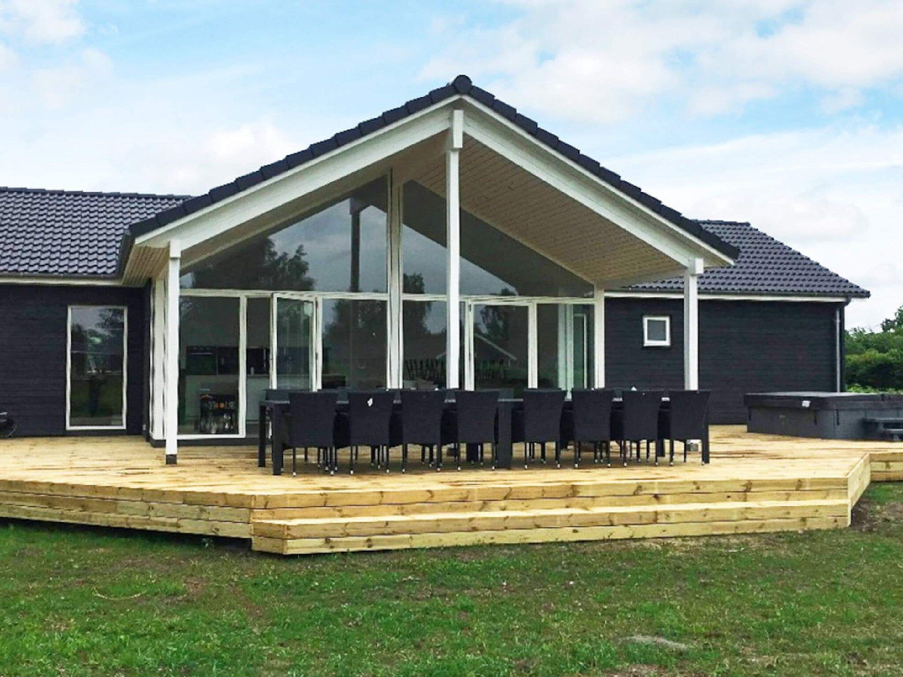 A covered outdoor seating area with a wooden deck and black chairs.