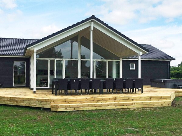 A covered outdoor seating area with a wooden deck and black chairs.