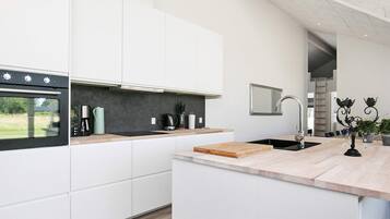 A modern kitchen with white cabinetry, a built-in oven, a coffee maker, and a wooden cutting board.